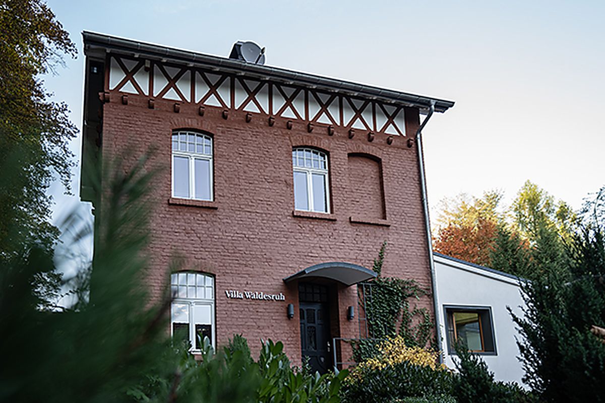 Die Villa Waldesruh im Abendlicht: ein Backsteinhaus mit Fachwerkgiebel, umgeben von Bäumen
