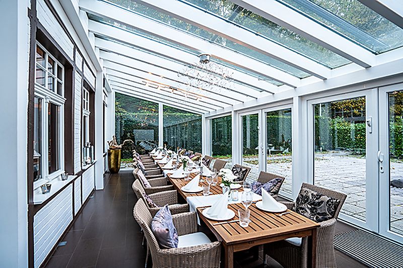 Der Wintergarten der Villa Waldesruh mit einer langen gedeckten Tafel und Blick in den Park